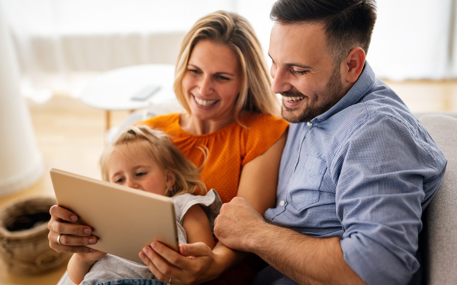 Une famille — deux parents et leur enfant — apprend ensemble à la maison avec une tablette, dans une ambiance chaleureuse
